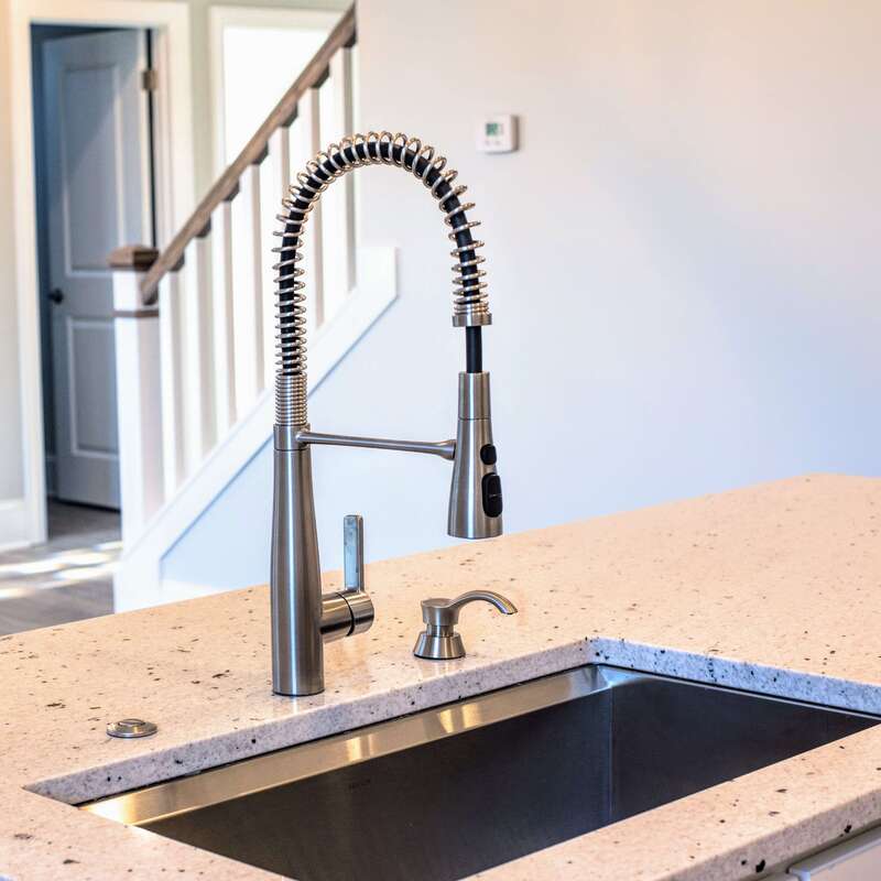 stainless steel gooseneck faucet and sink with matching built-in hand pump and quartz counter detail, staircase in background